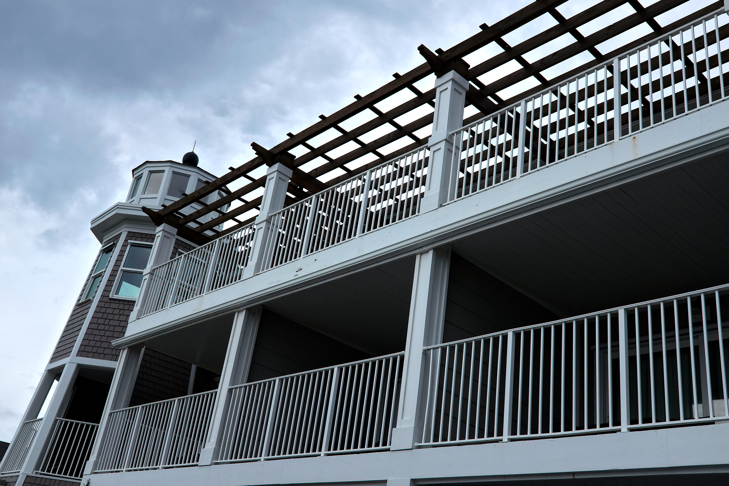 Exterior of The Lighthouse Inn in Kure Beach, North Carolina, featuring a lighthouse-style tower with signage and multiple balconies, and a cloudy sky.